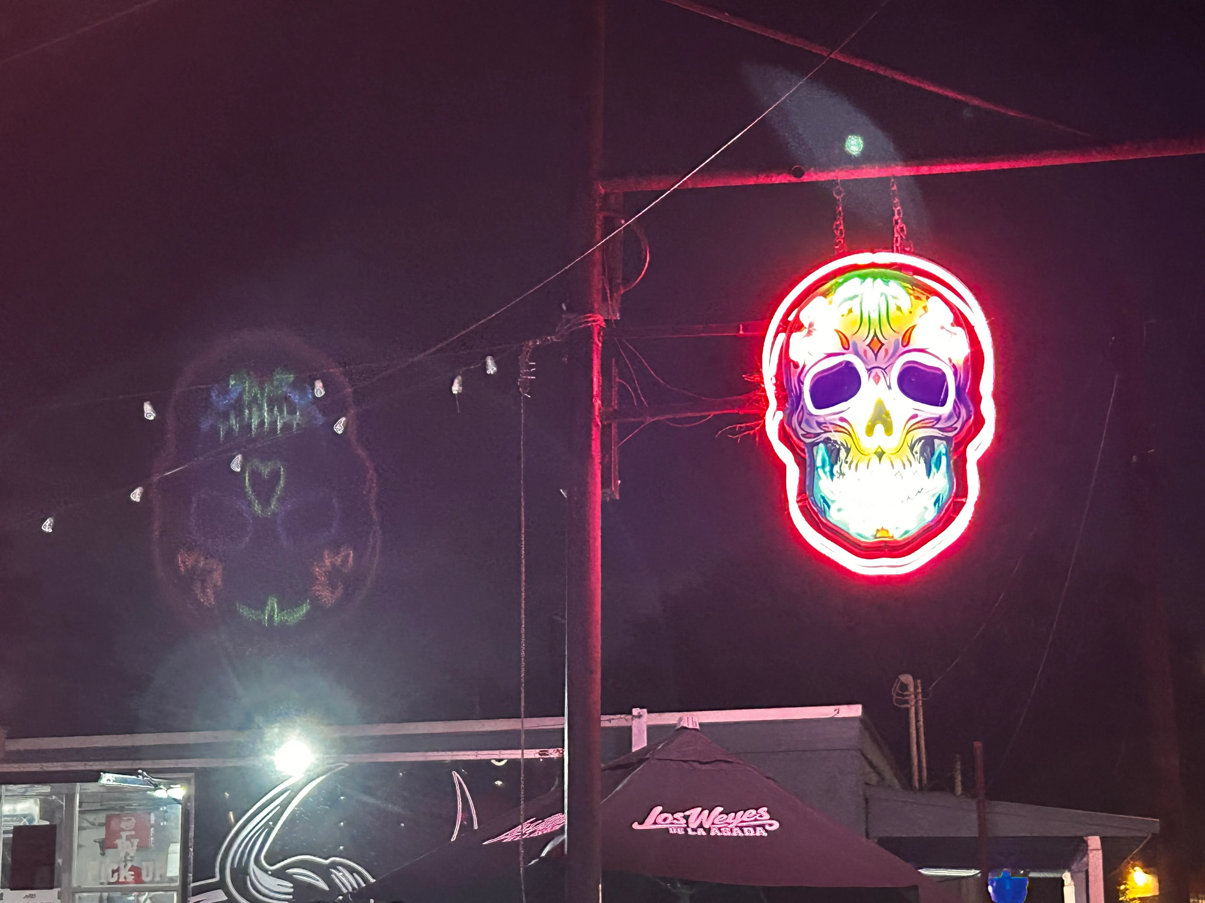 Neon sugar skull sign glowing against a dark night sky in San Antonio